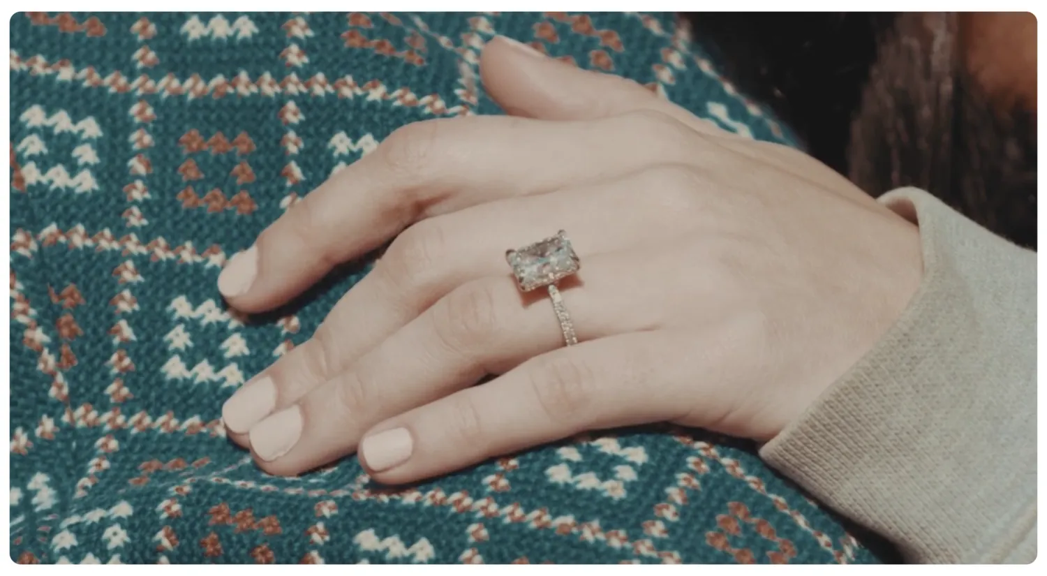 The finished ring on a hand resting on a patterned blanket — the last frame of the story.