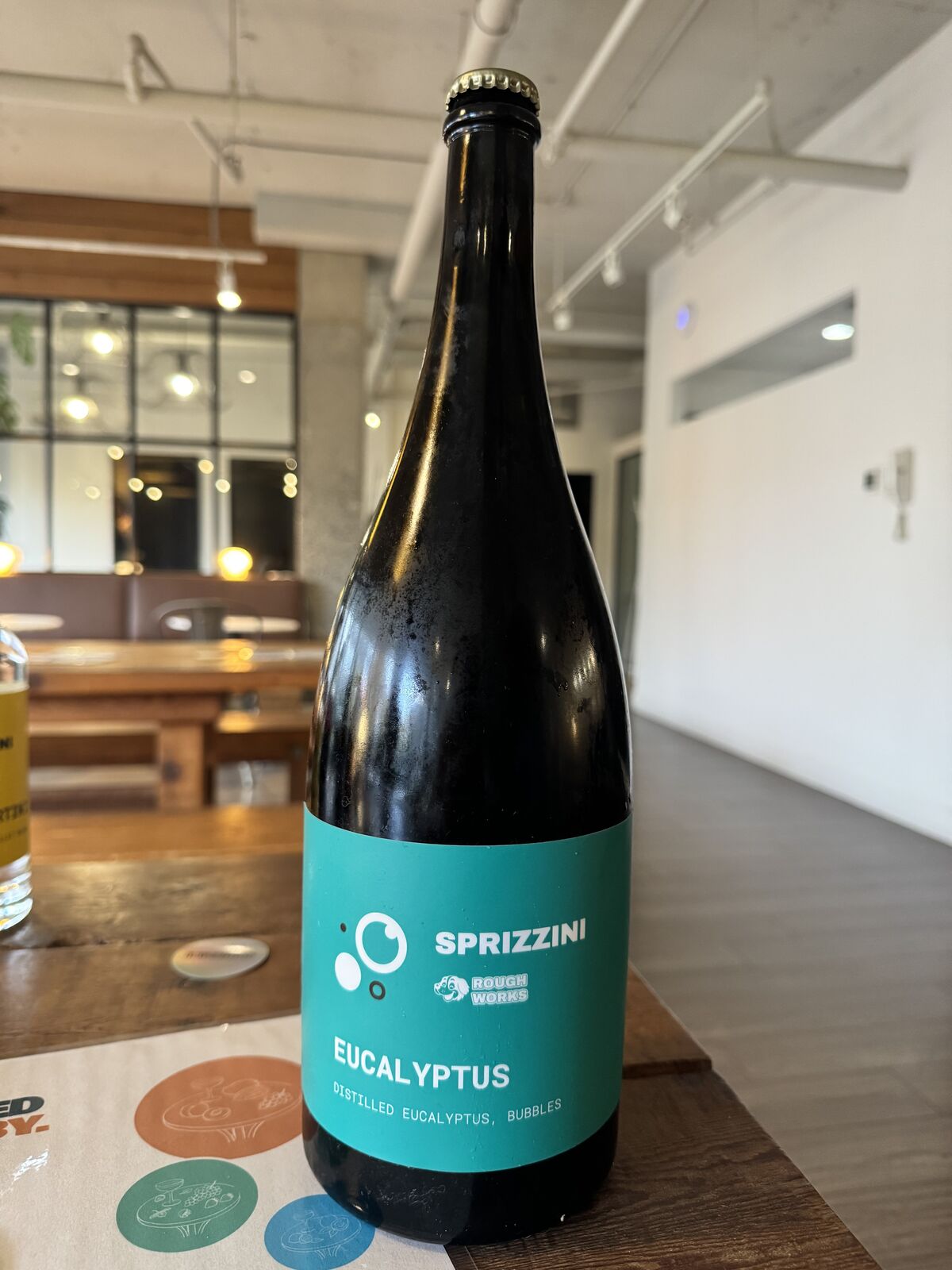 The Eucalyptus bottle, sea-green label, beside the drink coasters
