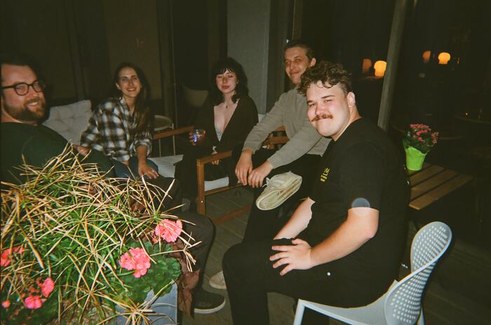 Five guests sitting together on the patio beside a planter of pink flowers