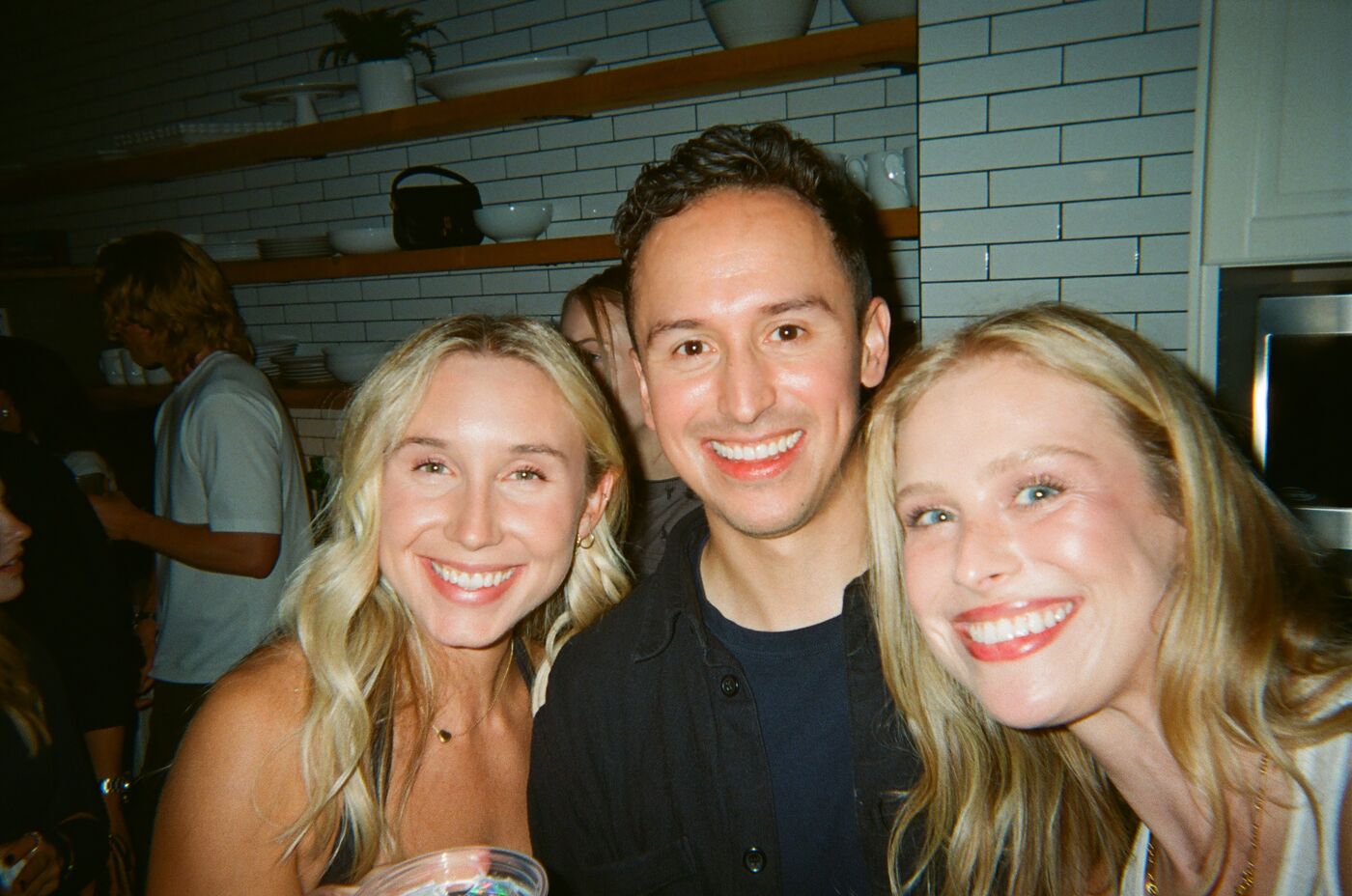 Three guests smiling cheek to cheek in the kitchen