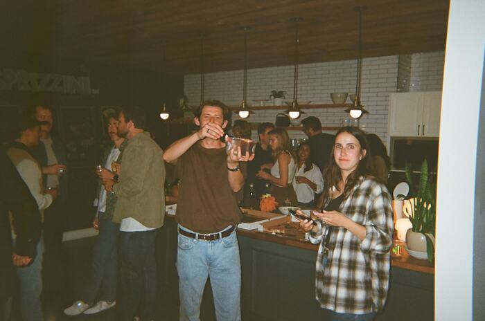 Guests around the kitchen island, one raising a cup to the camera