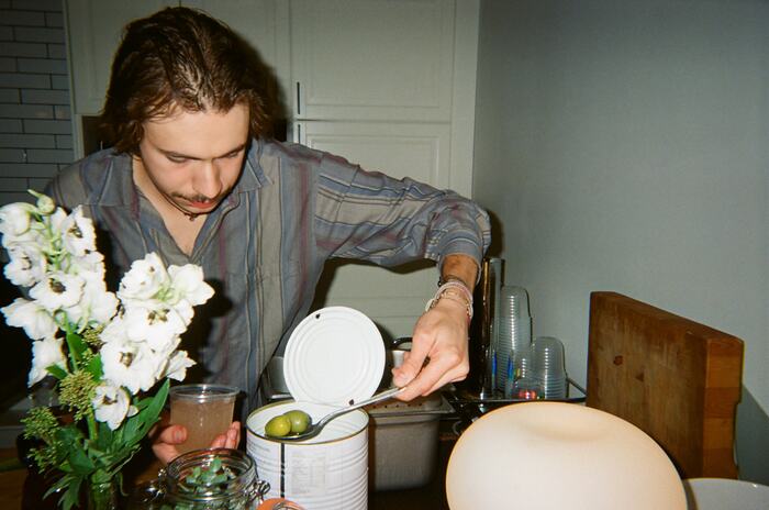 A guest spooning an olive out of a catering tin beside white flowers and a pale spritz