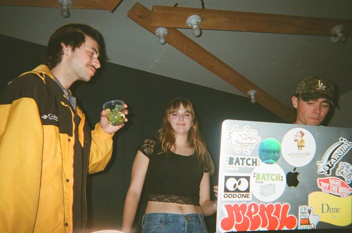 Guests behind a sticker-covered laptop, one holding a drink with lime