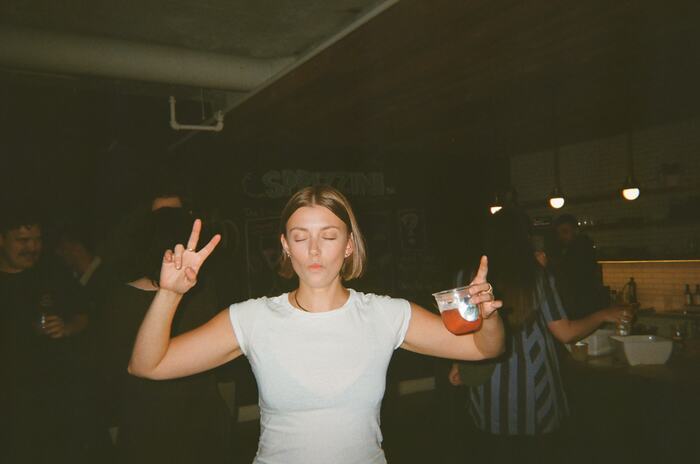 A guest in a white tee dancing with her eyes closed, arms up, a red drink in one hand