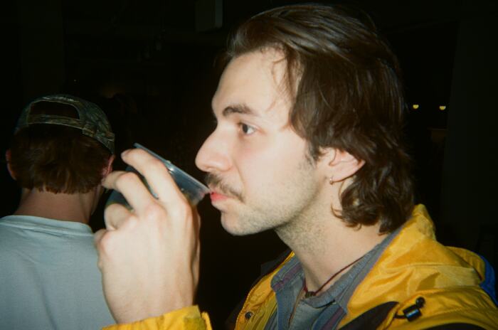 A guest in a yellow jacket drinking from a cup, in profile