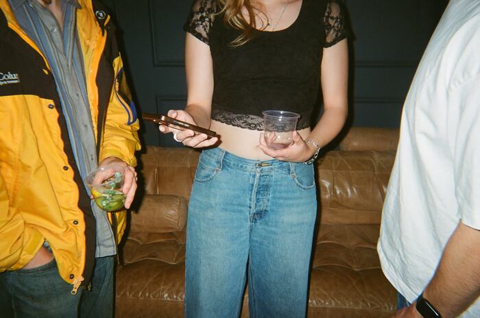 A guest holding a phone and an empty cup in front of the leather couch