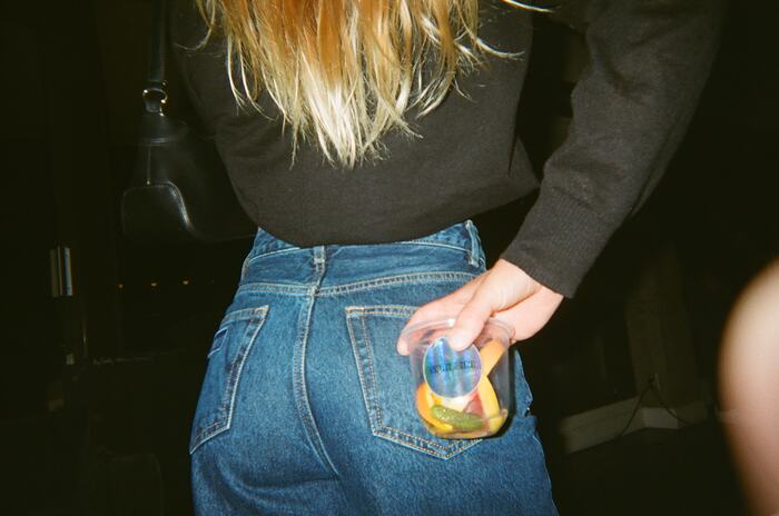 A guest seen from behind, holding a drink with orange against the back pocket of her jeans