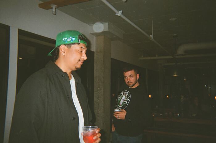 Two guests standing by a column, one holding a red drink