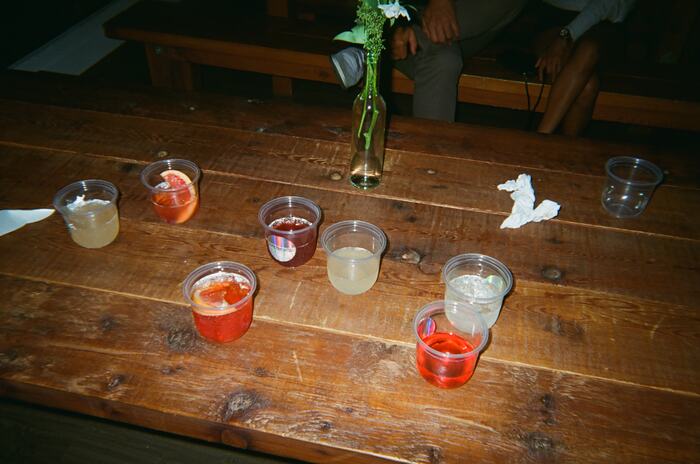 Eight cups of Sprizzini in reds and pale yellows scattered across the long wooden table