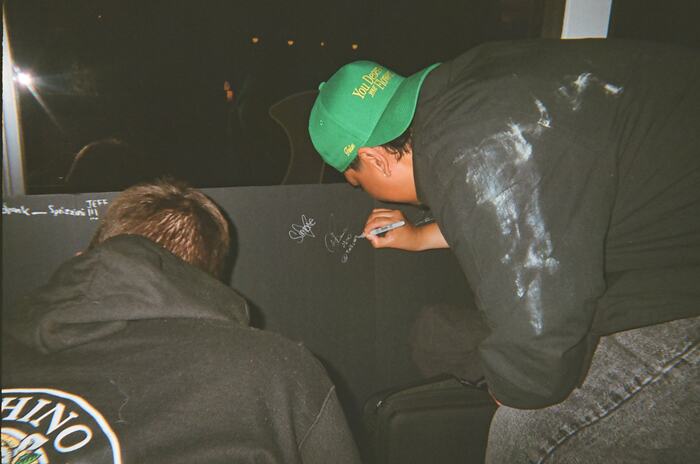 A guest in a green cap signing the black board in silver pen