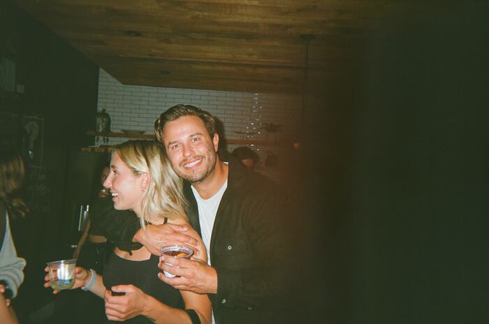 Two guests smiling with drinks, the edge of the frame washed out by a light leak