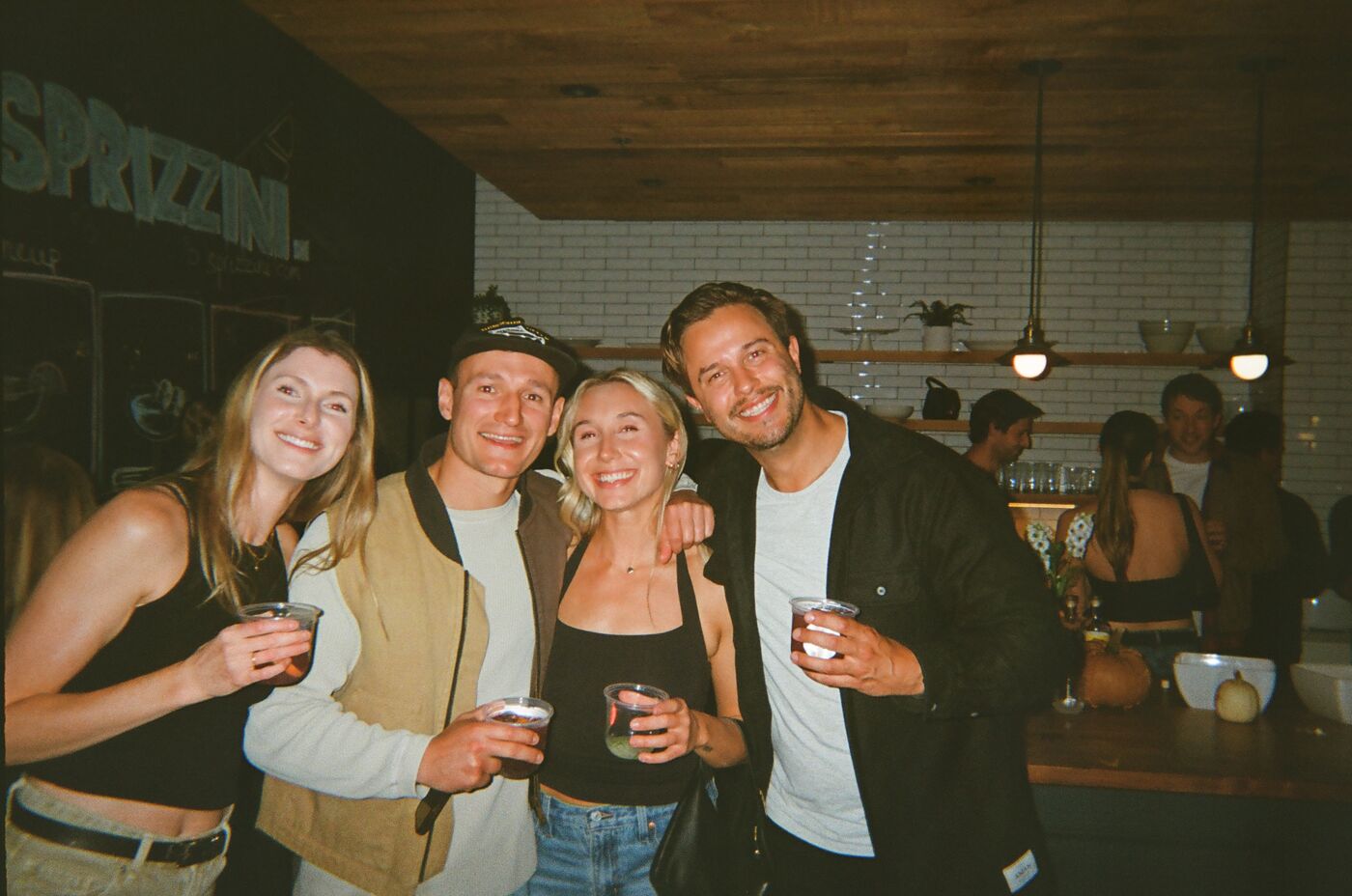 Four guests arm in arm in front of the kitchen, each holding a drink