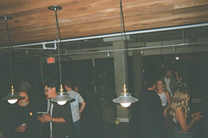 The room from the kitchen end, pendant lamps in front and guests across the floor