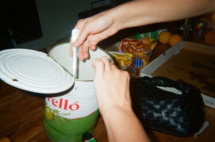 Hands reaching into a large tin of olives with a spoon
