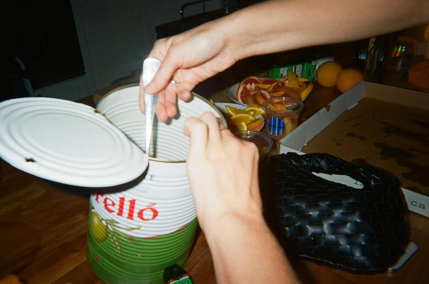 Hands reaching into a large tin of olives with a spoon