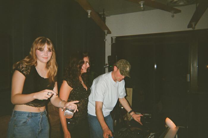 Two guests pointing at the decks while the DJ leans in