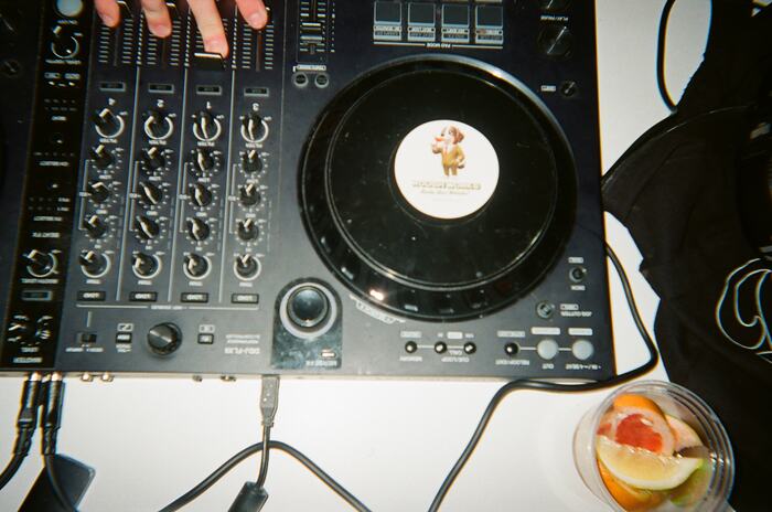 The DJ controller from above, fingers on the faders, citrus garnish beside it