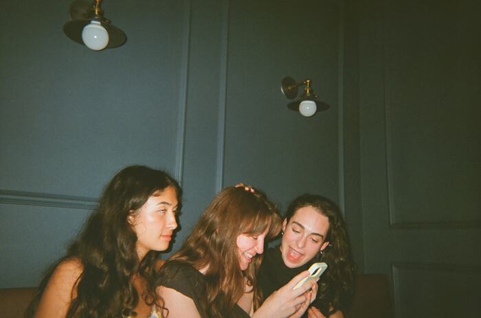 Three guests huddled over a phone on the banquette