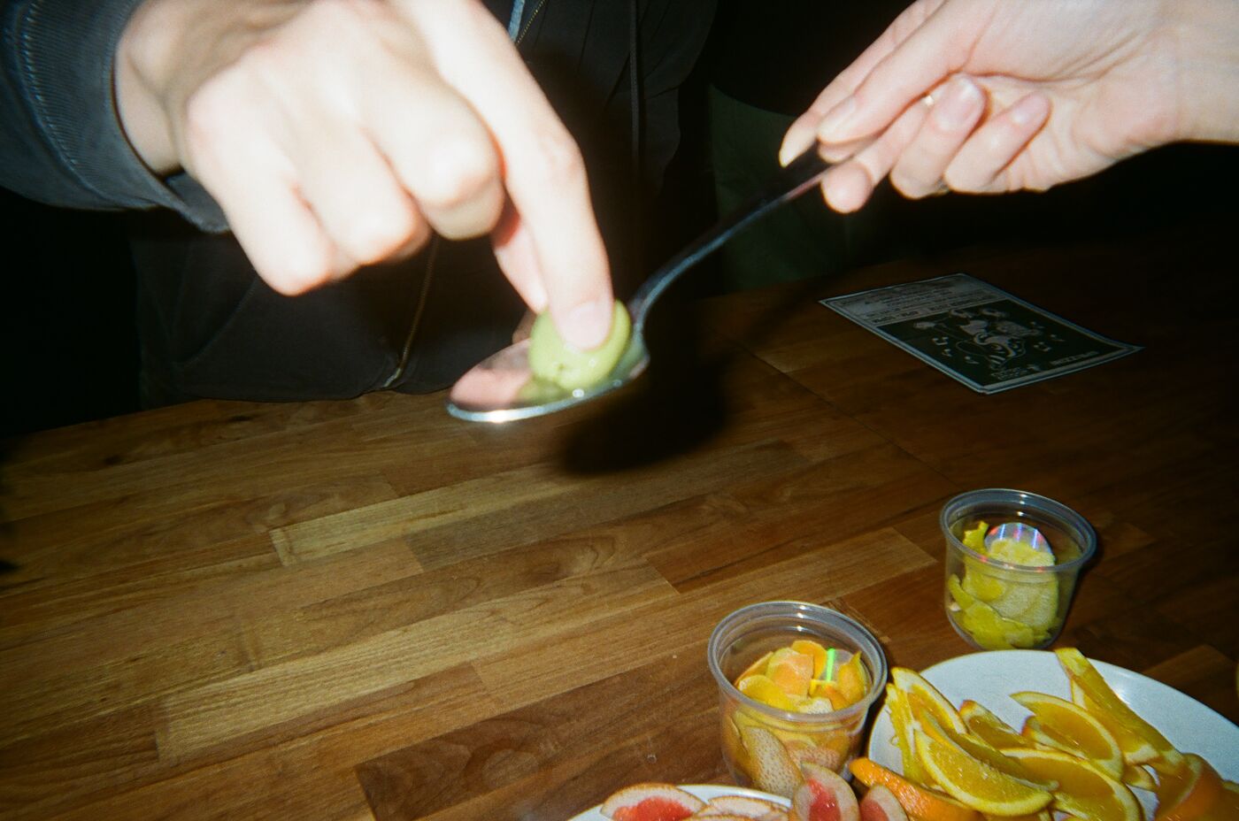 An olive balanced on a spoon above plates of sliced orange and grapefruit