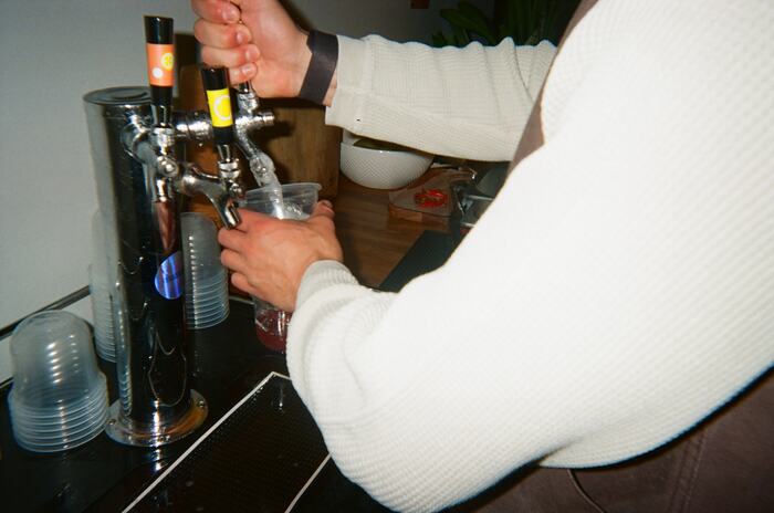 An arm in a cream knit pulling a tap to fill a cup