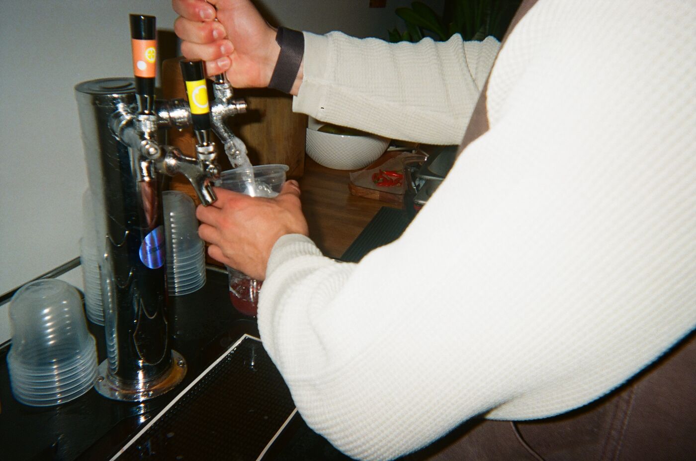 An arm in a cream knit pulling a tap to fill a cup