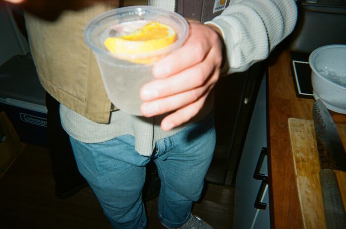 A hand holding a pale spritz with a wheel of orange, seen from above