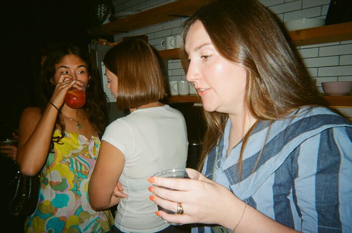 Three guests in the kitchen, one drinking a red drink