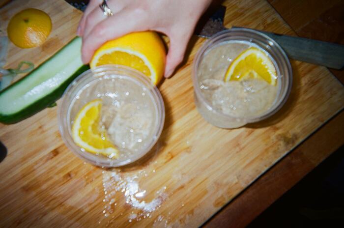 A hand squeezing an orange over two iced spritzes on a wooden board