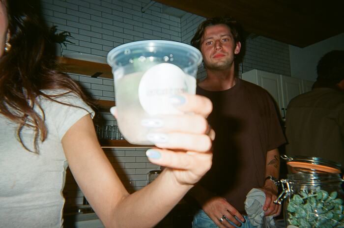 A hand holding a pale spritz with a holographic Sprizzini sticker up to the camera
