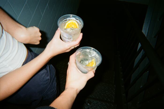 Two hands holding iced spritzes with orange over the stairwell