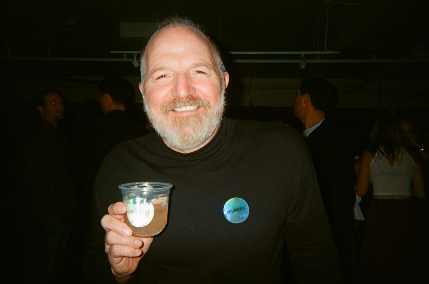 A guest in a black turtleneck beaming, holding up a cup with a Sprizzini sticker