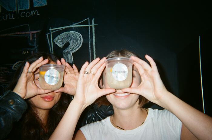Two guests holding cups with holographic Sprizzini stickers over their eyes