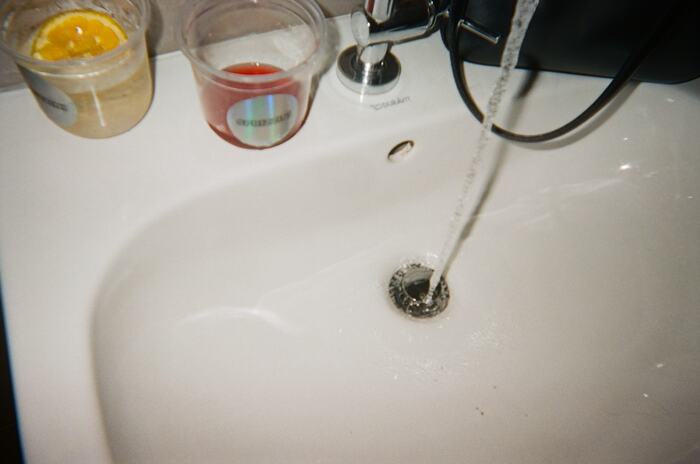 Two drinks resting on the edge of a washbasin with the tap running