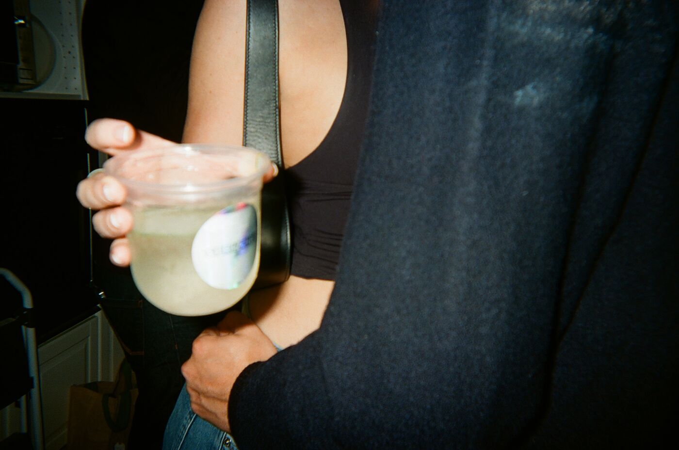 A hand holding a pale spritz with a holographic sticker