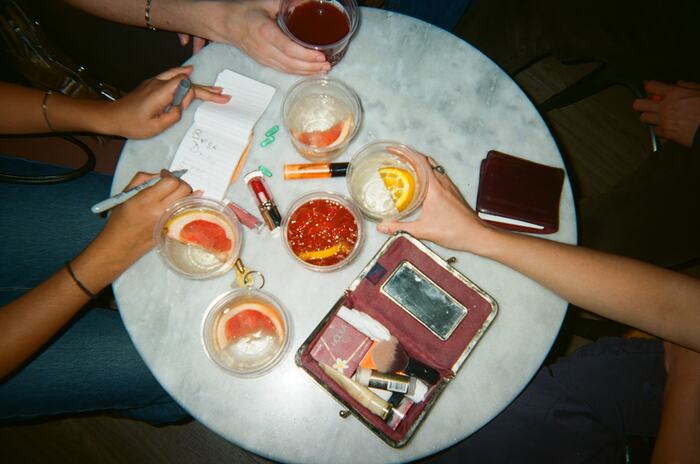A marble café table from above with five drinks, a notebook and hands reaching in