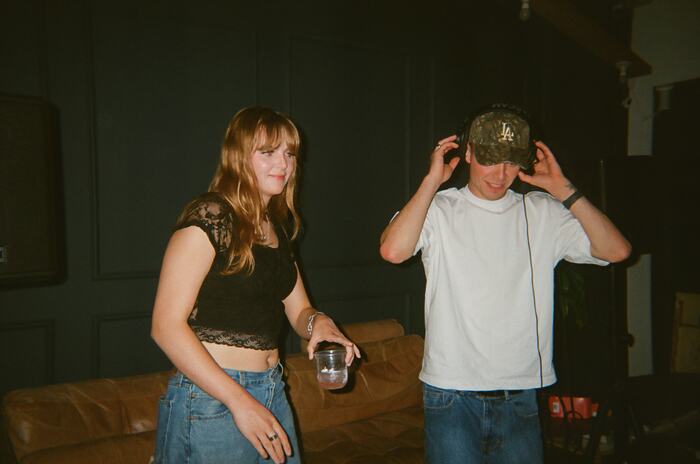 The DJ adjusting his headphones beside a guest holding a cup