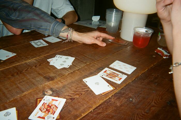 Playing cards spread across the long table beside a red drink