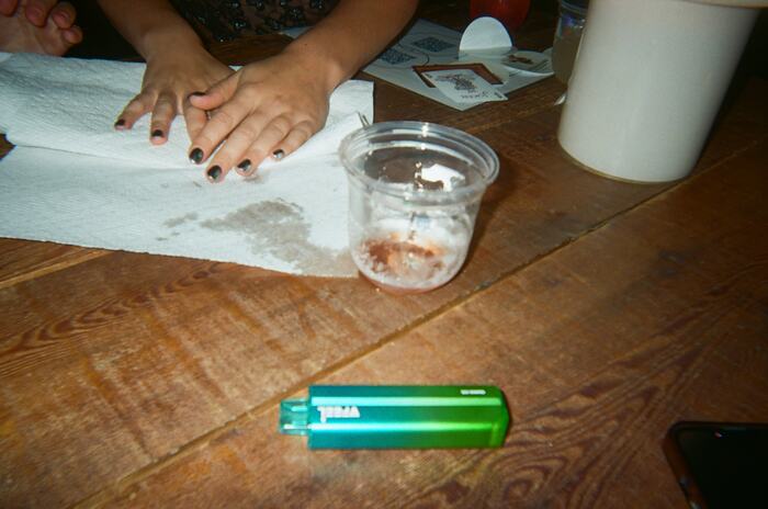 Hands pressing paper towel onto a spill on the long table beside an empty cup