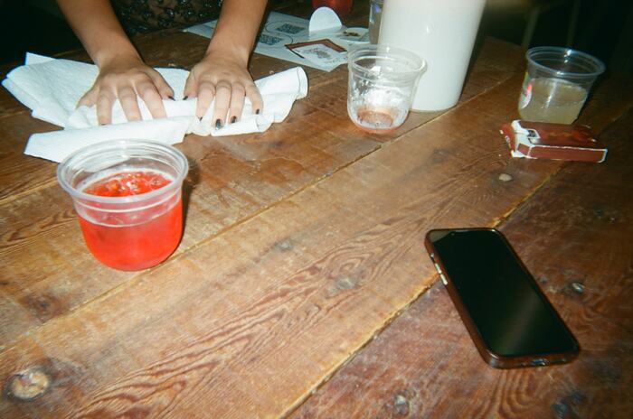 Hands mopping the long table with paper towel beside a red drink